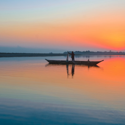 Enchanting Travels India Tours fisherman with his net and boat on the River Brahmaputra at Sunset