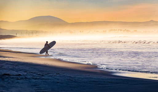 Early morning fog shrouds the coastline as this surfer enters the water in Coronado, California