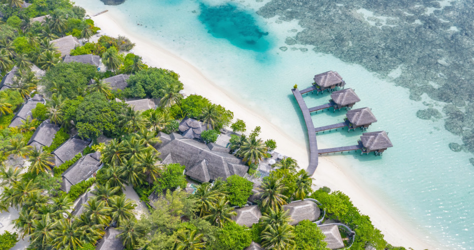 Aerial view of beautiful white sand beach, palm trees and villas, bungalows luxury beach scene of Maldives island