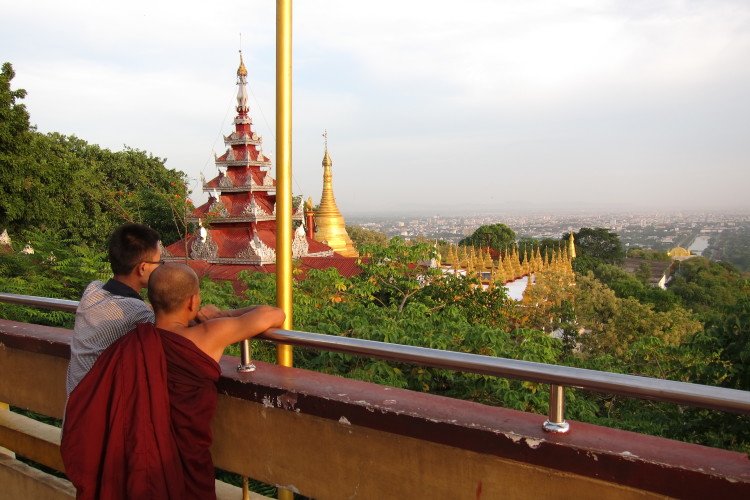 monk and boy at mandalay hill watching view on the city mandalay with golden pagoda in the background