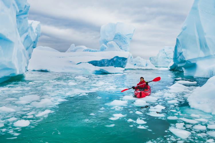 Man paddling on kayak between ice in Antractica, near Pleneau Island