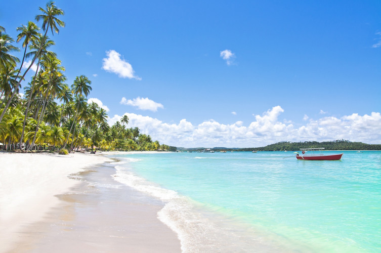 Strand Carneiros in Pernambuco, Brasilien: weißer Sandstrand mit Palmen, türkisblauem Wasser und einem roten Boot.