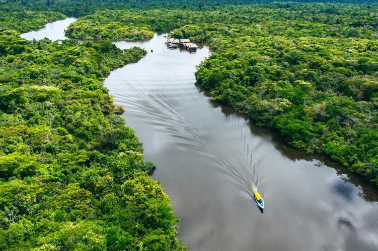 Luftaufnahme des Río Momón in Peru: Ein Boot fährt durch den Fluss, umgeben von dichtem Amazonas-Regenwald.