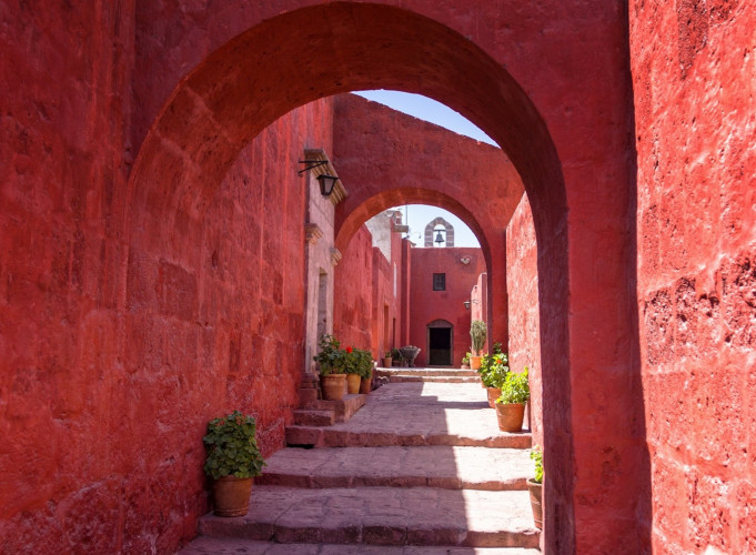 Enge Gasse mit roten Steinmauern und Rundbögen im Kloster Santa Catalina, Arequipa, Peru. Treppen, Topfpflanzen und Glockenturm.