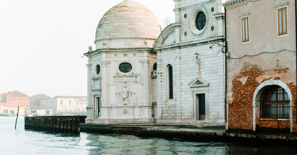 Historic Venetian church with white marble dome and brick facade along a canal waterfront in Italy.