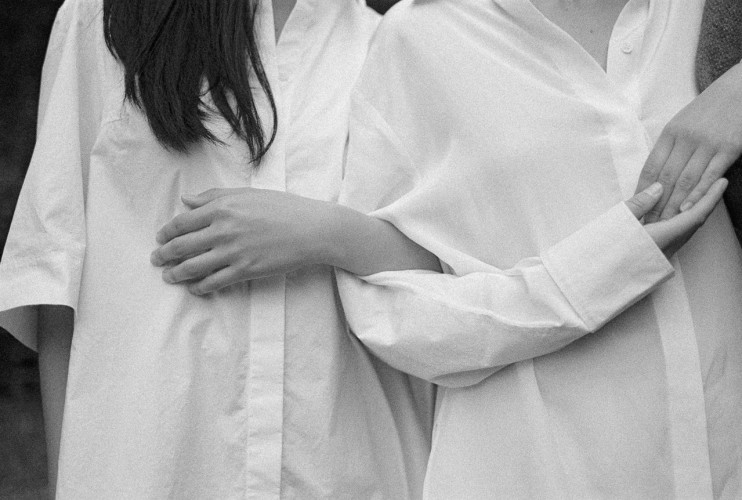 Three people in white button-down shirts embracing, arms wrapped around each other, shot in black and white.