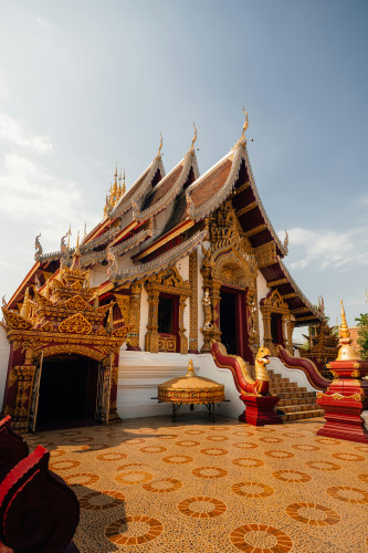Thai Buddhist temple with ornate gold and red decorations, tiered roofs, guardian statues, and a patterned mosaic courtyard.