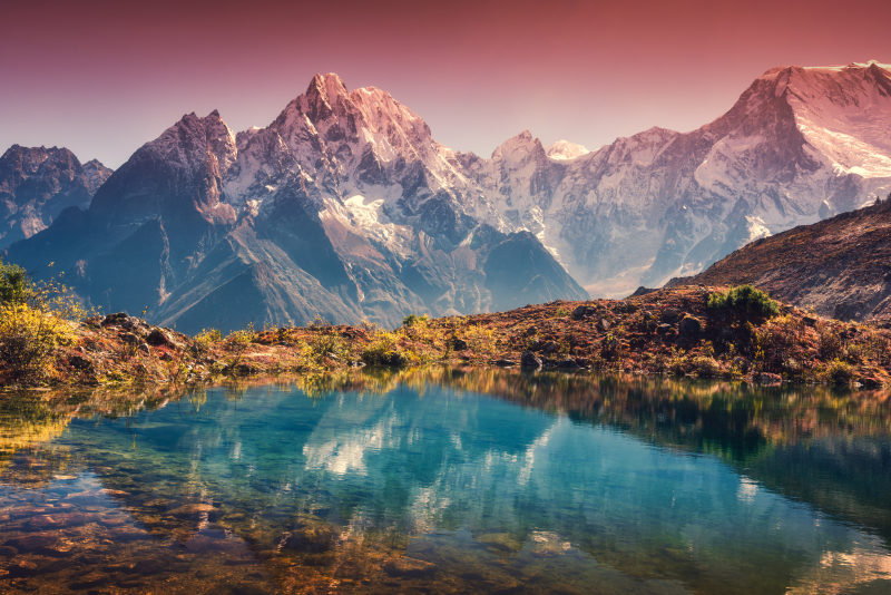Wunderschöne Landschaft mit hohen Bergen und schneebedeckten Gipfeln, roter Himmel, der sich im See spiegelt Bergtal mit Spiegelung im Wasser bei Sonnenuntergang Nepal
