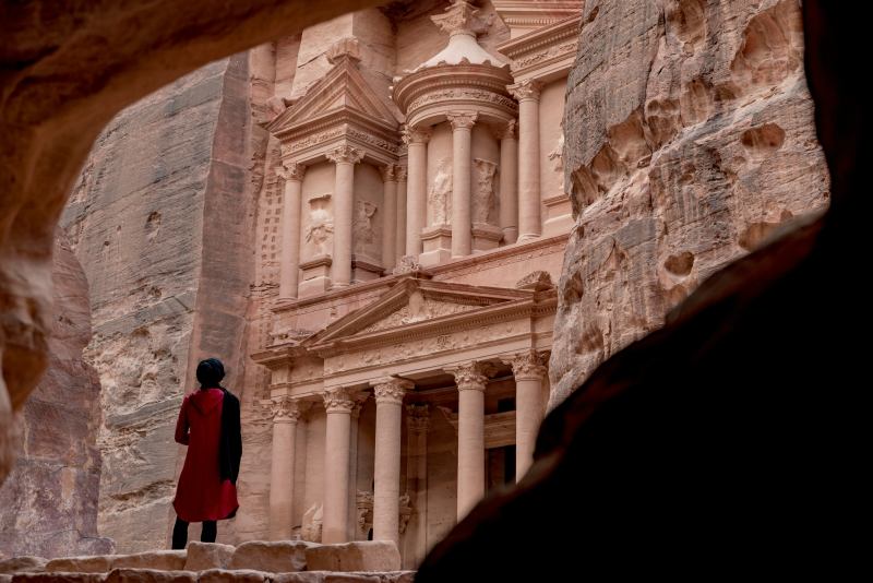 Woman in red coat standing in front of white concrete building during daytime middle east