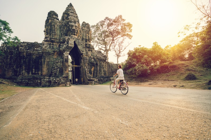 Young-woman-traveling-in-Cambodia-visiting-the-temples-of-Angkor-wat-complex-by-bicycle