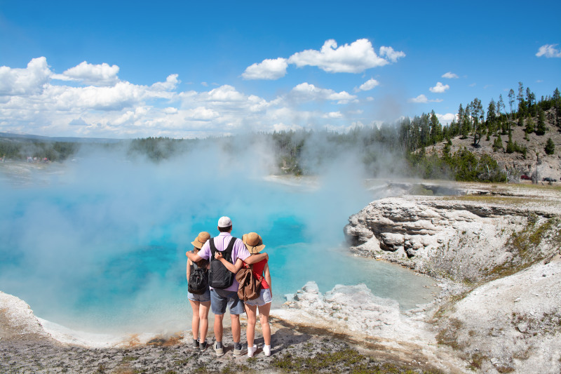 Family relaxing and enjoying beautiful view of gazer on vacation hiking trip-Father with arms around his family-Excelsior Geyser from the Midway Basin in Yellowstone National Park Wyoming USA