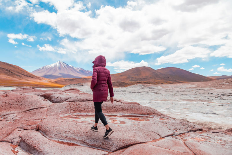 a-woman-in-a-red-jacket-is-walking-on-a-rock