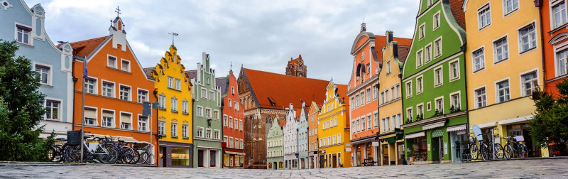 Enchanting Travels Traditional colorful gothic houses in the Old Town of Landshut, historical town in Bavaria by Munich, Germany, reflecting in a rain puddle