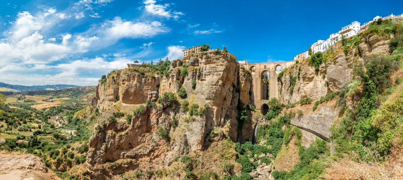 Tourists taking pictures to the Puente Nuevo bridge and the houses built on the edge of the cliff, in the ancient city of Ronda, Spain