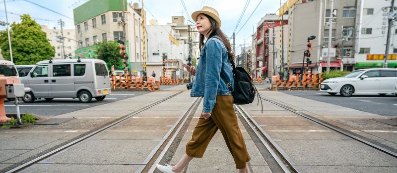 relaxed woman walking across the railroad holding her phone in osaka city in japan