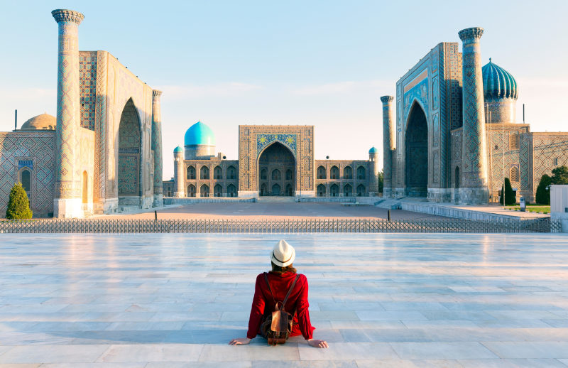 Touristin mit Hut und rotem Kleid, die auf dem Registan sitzt