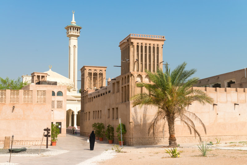 Woman-in-traditional-muslim-black-dress-in-old-arabic-city-district-with-mosque-minaret-on-background