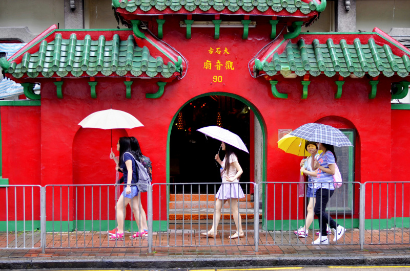 man and woman holding umbrella walking on sidewalk during daytime hong kong