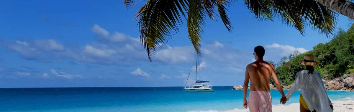 Couple walking along the beach with their charter yacht in the background
