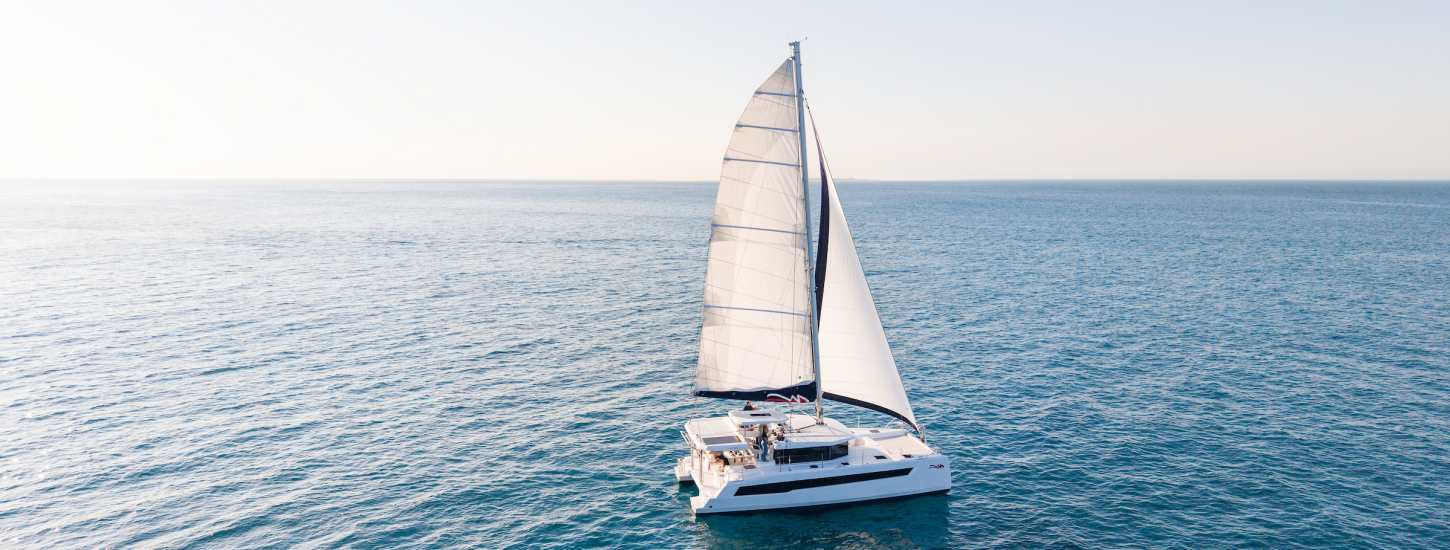 A sailing catamaran under full sail on open water.
