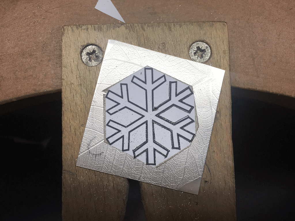 Debossed silver sheet sitting on a benchpeg showing paper template ready for cutting out