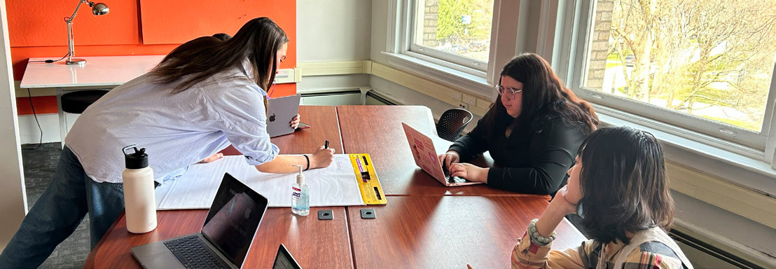 Students working on a laptop and large pad of paper across a table