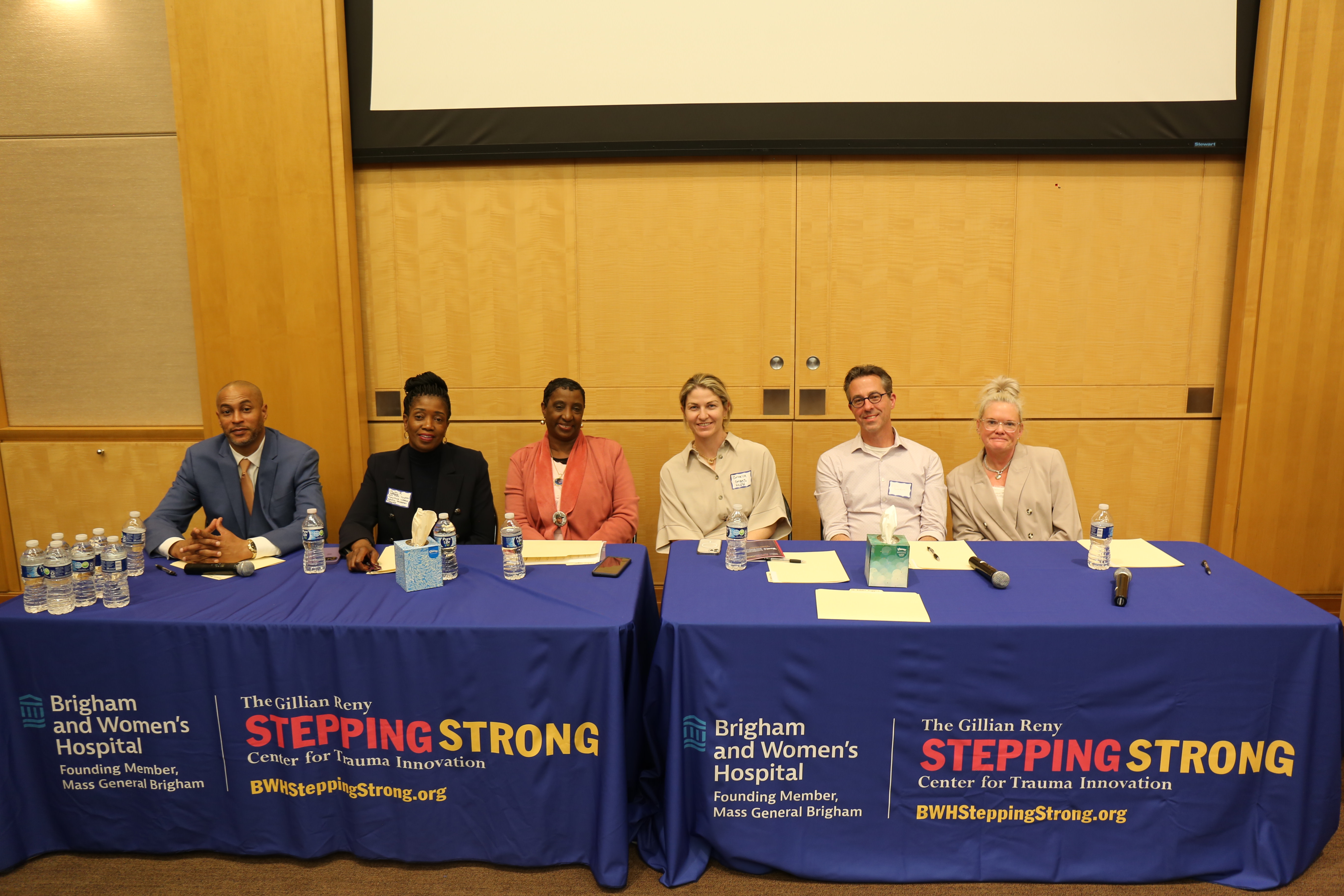 Six panelists seated at a blue-clothed table, posing for the camera