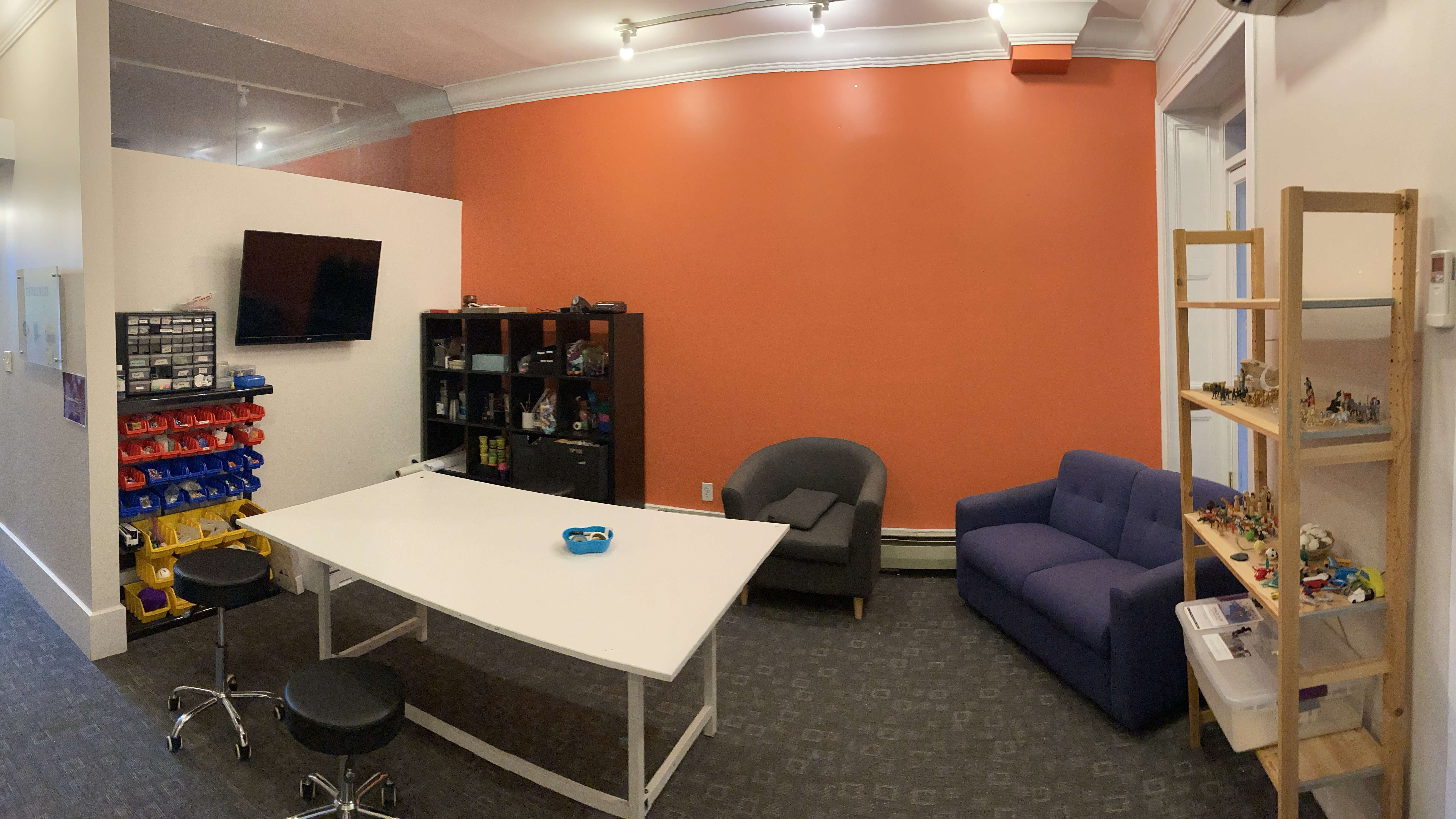 A room with an orange wall, a prototyping table, and shelves of materials