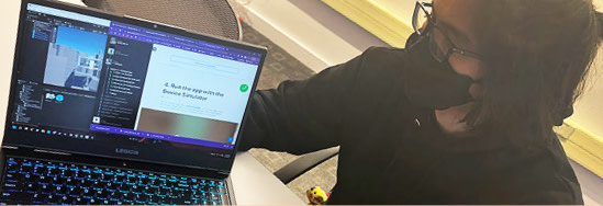 A student wearing a facemask and holding a laptop