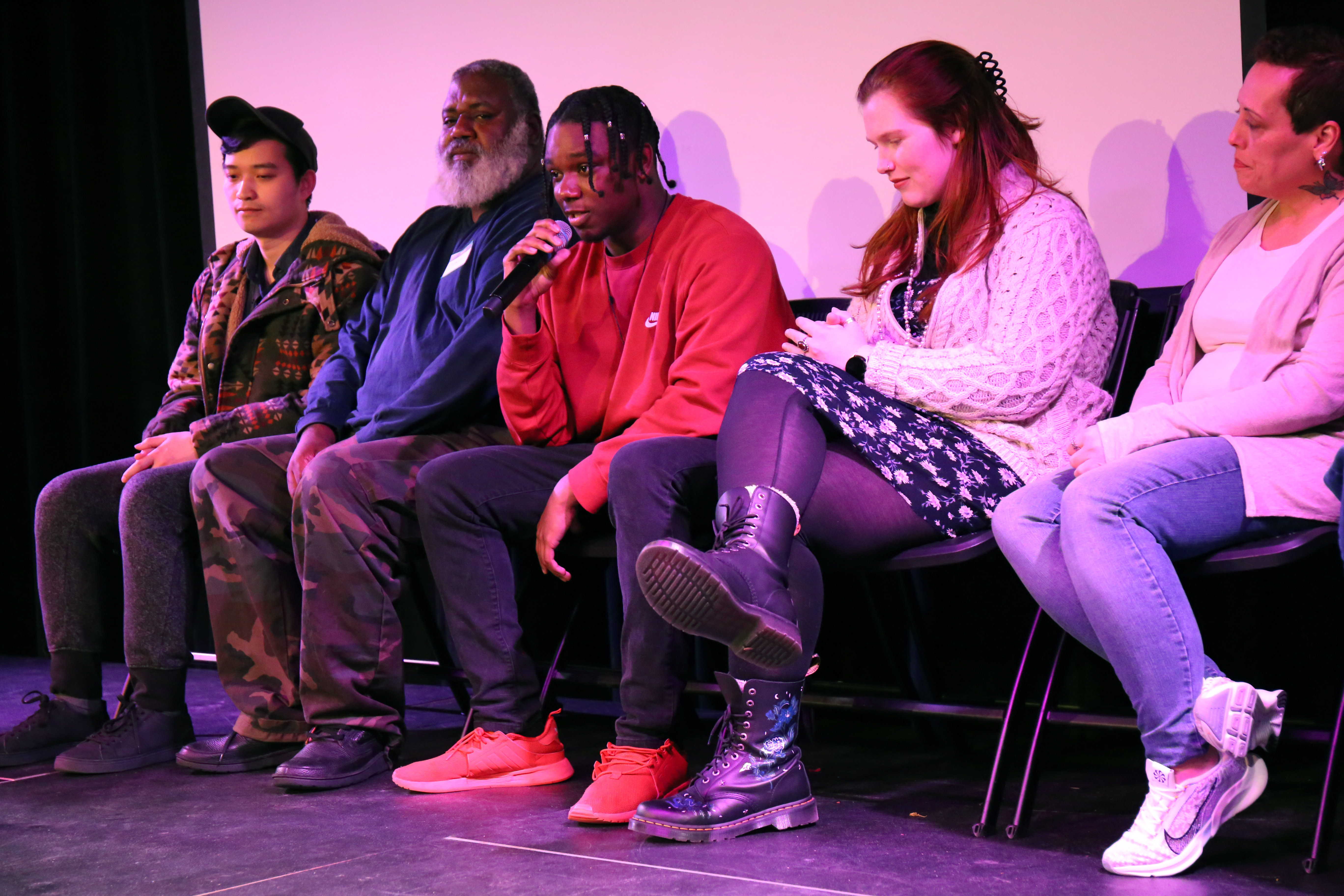 A gathering of five individuals seated on stage, one of whom is speaking into a microphone