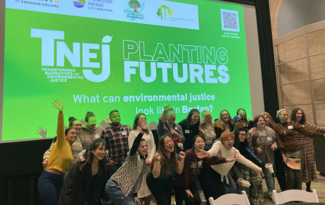 A crowd of posing studio participants in front of a projection of the TNEJ Planting Futures logo