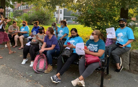 People in blue t-shirts and facemasks gathered around a park bench