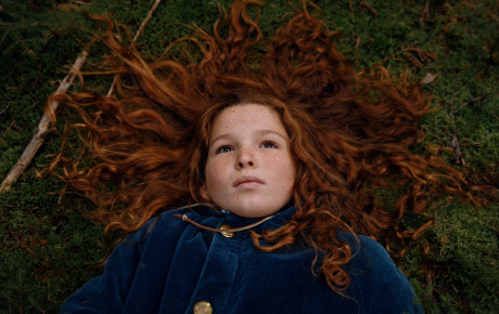 A still from the film King Coal, with a young girl with red hair laying on the grass