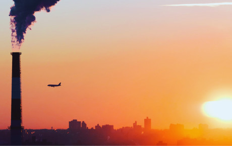 A plane flying near a smokestack during sunrise or sunset