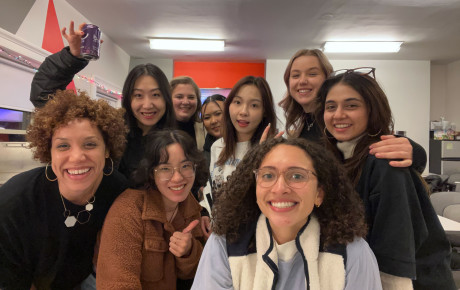 A gathering of nine individuals closely huddled to take a selfie together