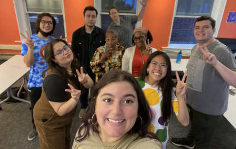 Eight individuals posing for a selfie and giving the camera peace signs