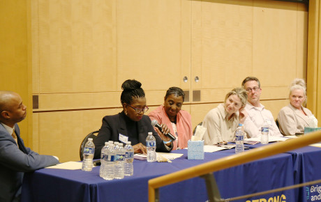 Six panelists seated at a table with a blue tablecloth; one is holding a microphone