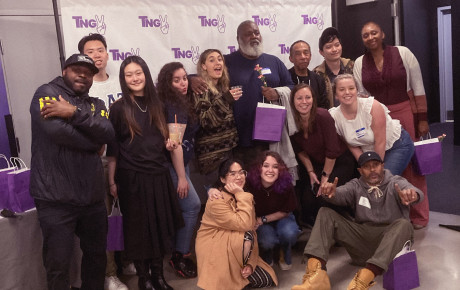 Fourteen individuals posing in front of a banner reading "TNGV"