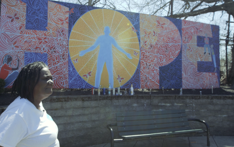 An individual standing in front of a mural which reads "HOPE"