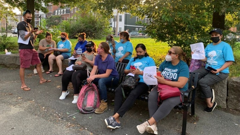 People in blue t-shirts and facemasks gathered around a park bench