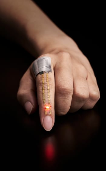 The electric current from a flexible battery placed near the knuckle flows through the conductor and powers the LED just below the fingernail. (Image courtesy of Someya Laboratory.)