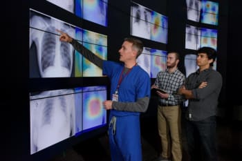 Radiologist Matthew Lungren, left, meets with graduate students Jeremy Irvin and Pranav Rajpurkar to discuss the results of detections made by the algorithm. A tool the researchers developed along with the algorithm produced these images, which are similar to heat maps and show the areas of the X-ray most indicative of pneumonia. (Image courtesy of Stanford University/L.A. Cicero)