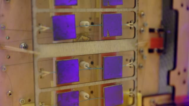 This image shows the underside of the gripper. The squares of the gecko-inspired adhesive are glowing as they grip a piece of glass that is lit purple. (Image courtesy of Kurt Hickman/Stanford News Service.)