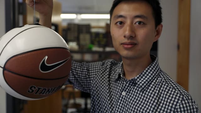 Hao Jiang, graduate student in the Cutkosky lab and lead author of the paper, shows a basketball being gripped by the gecko-inspired adhesive. (Image courtesy of Kurt Hickman/Stanford News Service.)