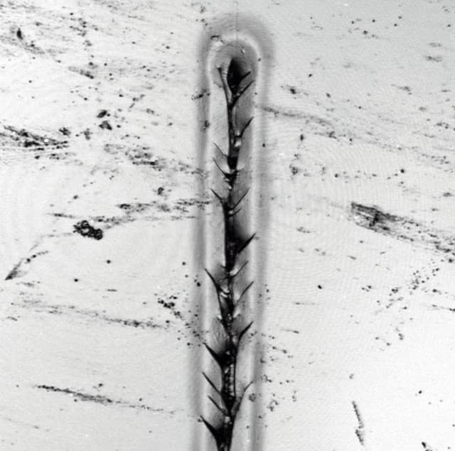 Photomicrograph showing the result of a NIST nanoscale scratch test on a sample of automobile clearcoat material. The scratch, which shows fractures radiating from the line of impact, is 20 micrometers wide, 150 micrometers long and 2 micrometers deep (A micrometer is a millionth of a meter or about half the length of an average E. coli bacterium.). (Image courtesy of NIST.)