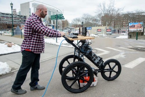 Postdoctoral student Dylan Burns wheels the cognitive ground penetrating apparatus over a paved area to obtain data on the structures beneath. (Image courtesy of Brian Jenkins.)