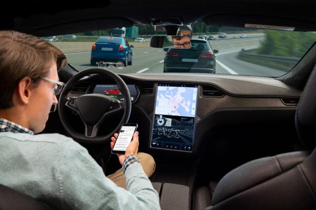 Checking news on a smartphone while the car is driven by an autopilot. Stock photo.