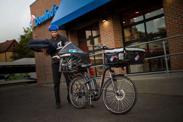 Cheaper by the dozen. Domino Pizza rolls out e-bike delivery. Modified Rad Power bikes fitted with the company's insulated cargo containers on the front and back with capacity for 12 large pizzas. (Picture courtesy of Domino.)