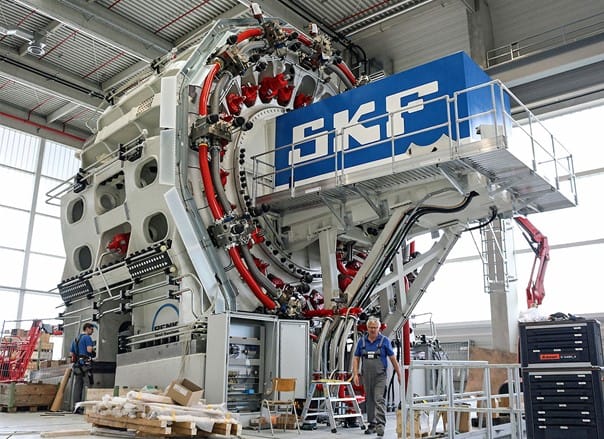 SKF has invested 40 million euros in the Sven Wingquist Test Center, the world’s most powerful large-size bearing test centre, situated in Schweinfurt, Germany. In the center’s futuristic-looking twin buildings, two huge new test rigs can drive and test large-size bearings to their absolute limits. The largest of the rigs is the first test rig in the world that can not only test a single wind energy bearing (with an outside diameter of up to six meters), but also the complete bearing assembly—including adjacent customer components. With overall dimensions of about 9 x 11 x 8 m, the giant rig weighs around 700 tonnes. It is equipped with a massive number of 64 radially and axially arranged cylinders, which can develop several meganewtons of dynamic loads.