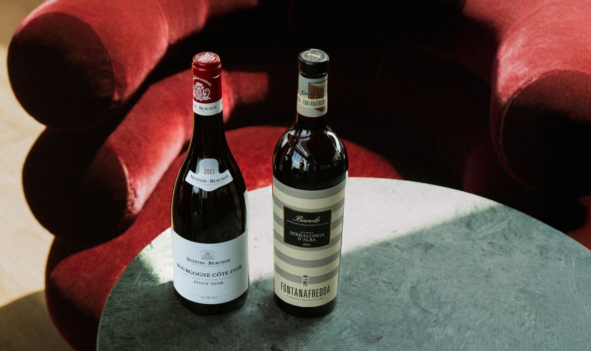 Two bottles of fine wines which are on a table next to a red lounge chair